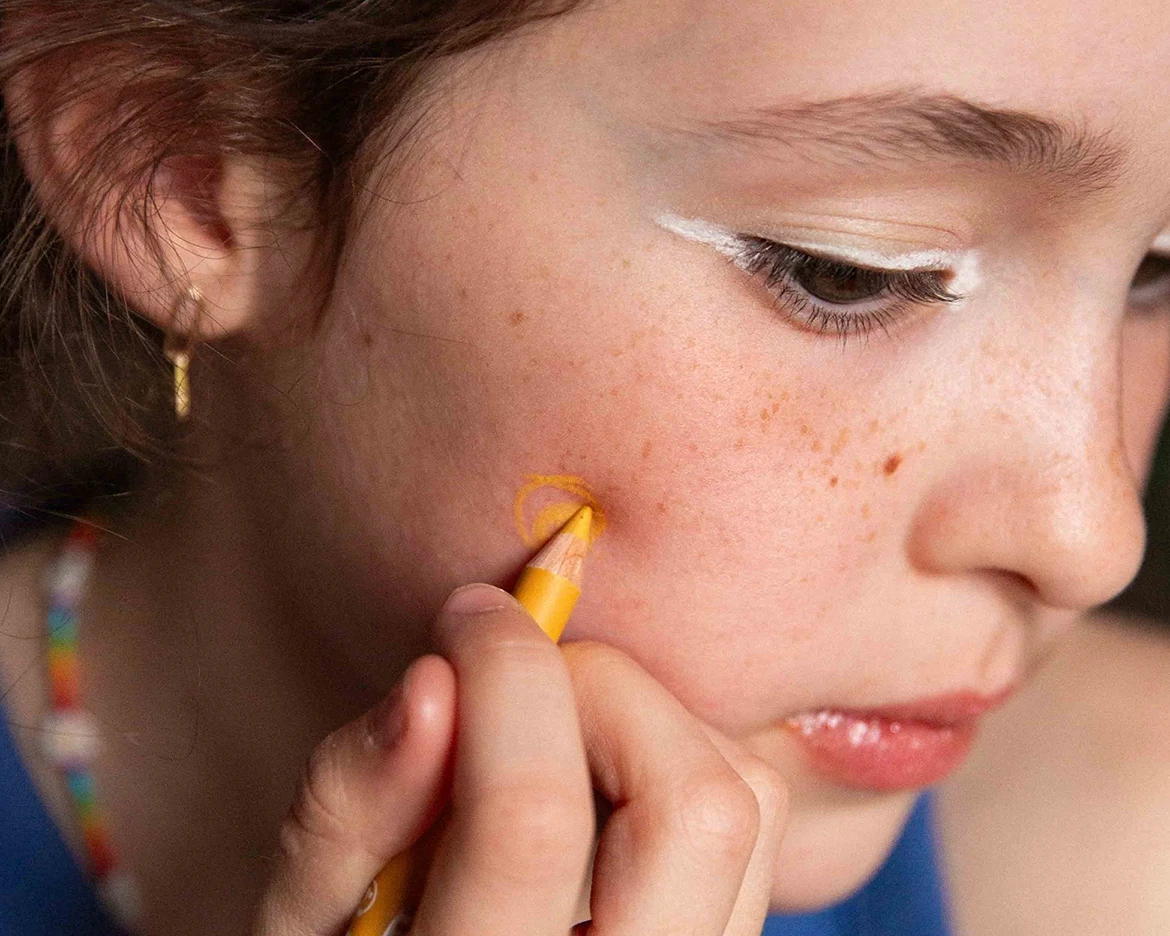 child applying yellow crayon to his cheek