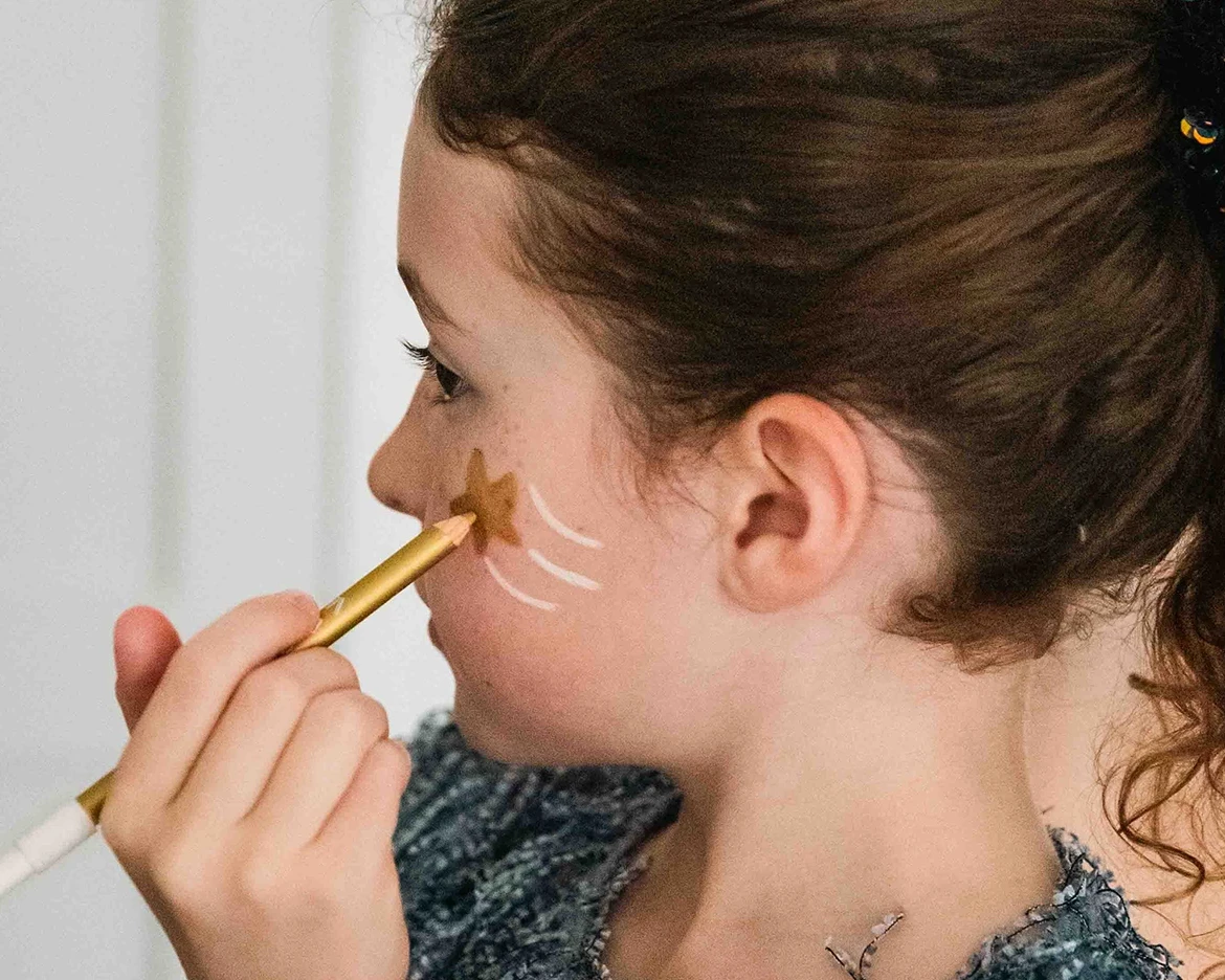 child applying gold crayon to her cheek