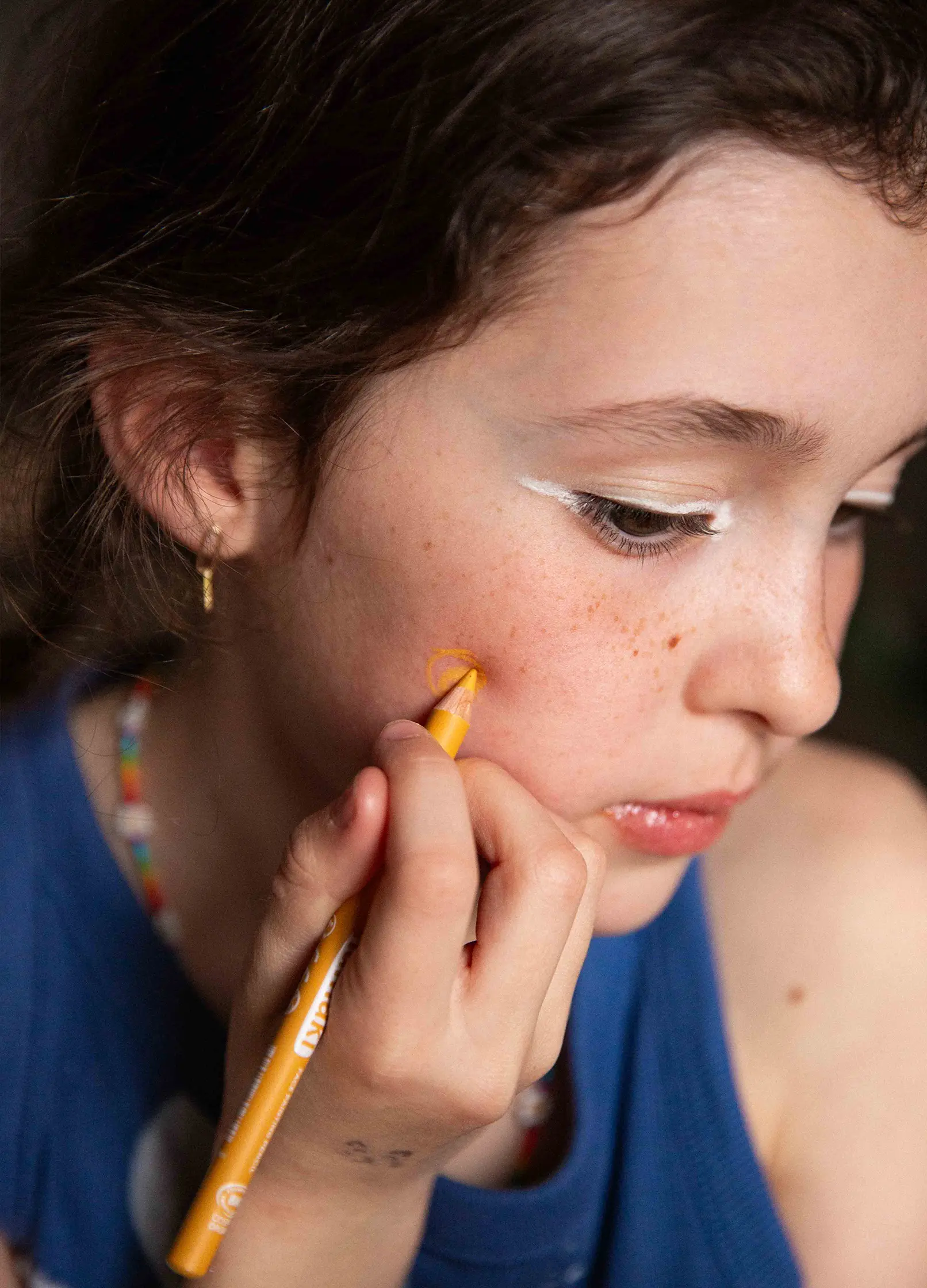 petite fille qui se maquille la joue avec un crayon fin