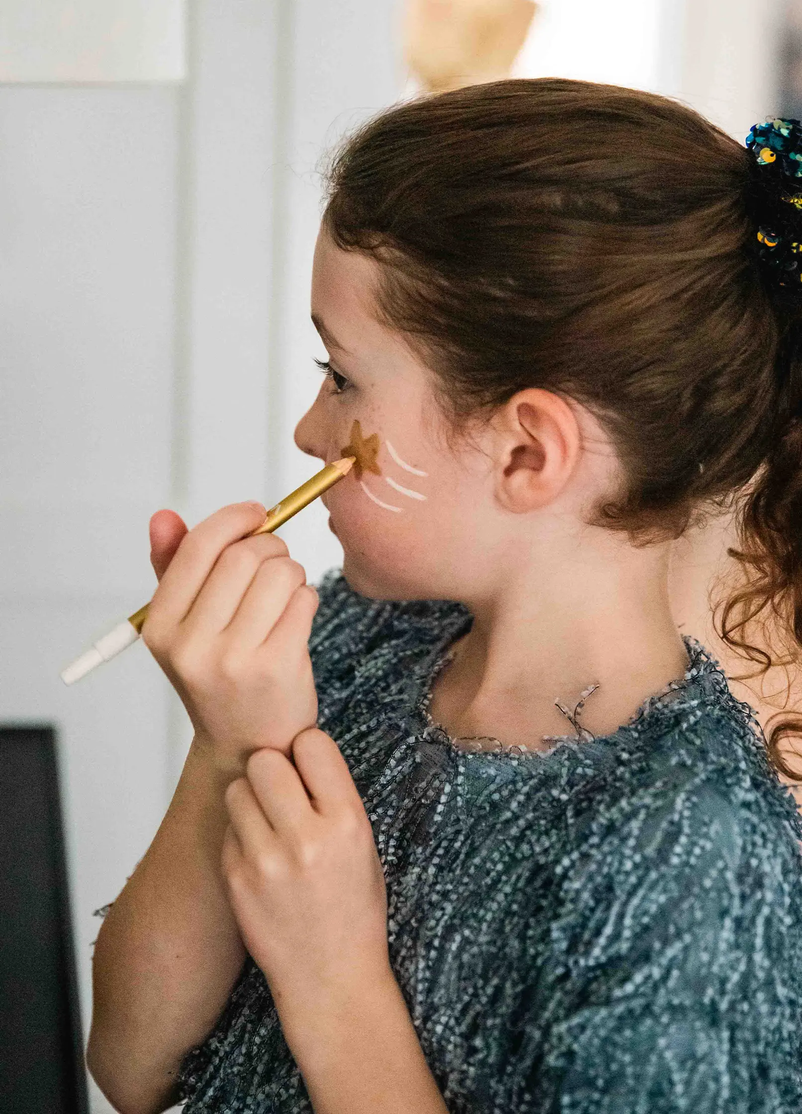 petite fille qui se maquille la joue avec un crayon fin