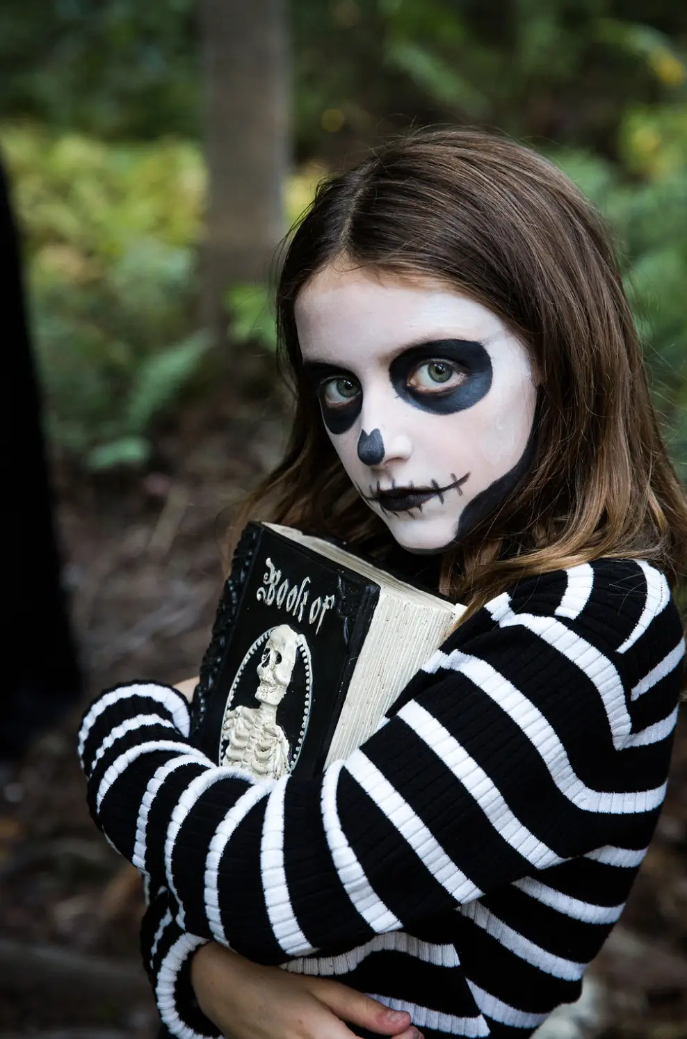 petite fille tenant un grimoire avec un maquillage d'Halloween